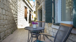 A narrow courtyard with stone walls, a round table with chairs, and a window with green shutters. - Authentic Luxury Rooms (Split)