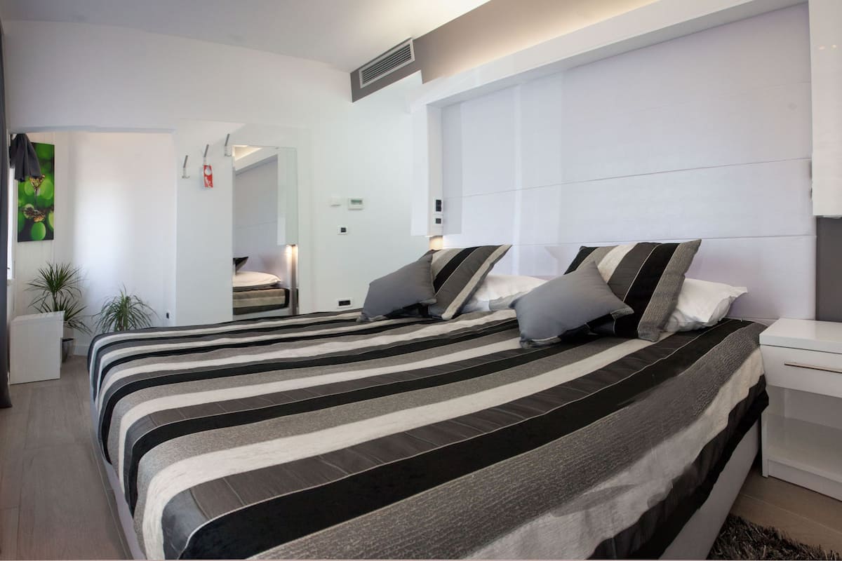 A modern hotel room with a large bed, bedside tables, a mirror, and a potted plant.