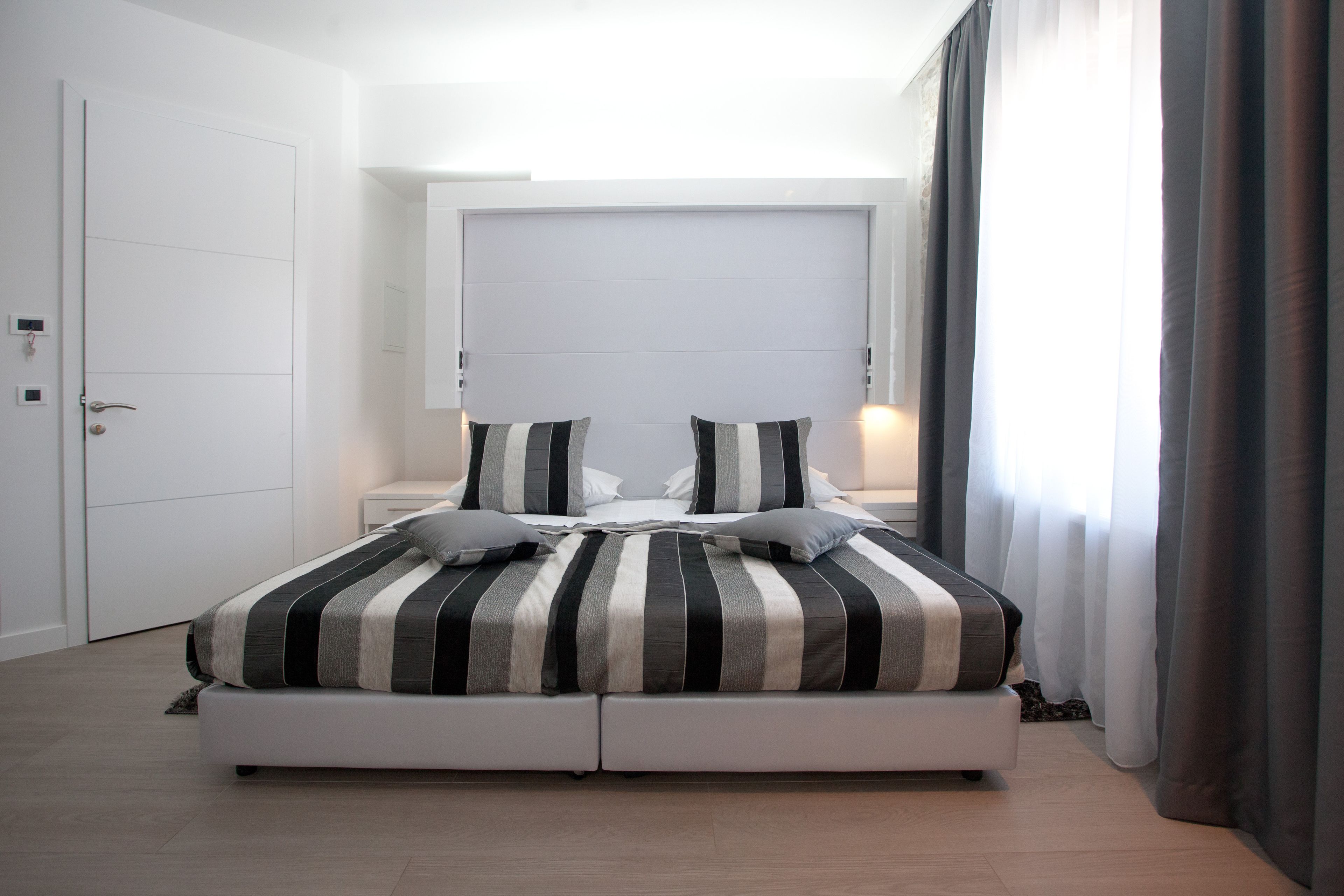 A modern bedroom with a large bed, a white wardrobe, and a nightstand.