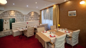 A dining area with tables set for four, cushioned seating, stone walls, and a large window with curtains. - Authentic Luxury Rooms (Split)