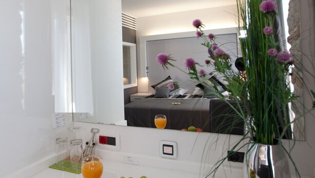 A hotel room with a white countertop, a plate of fruit, a glass of orange juice, and a vase with flowers. - Authentic Luxury Rooms (Split)
