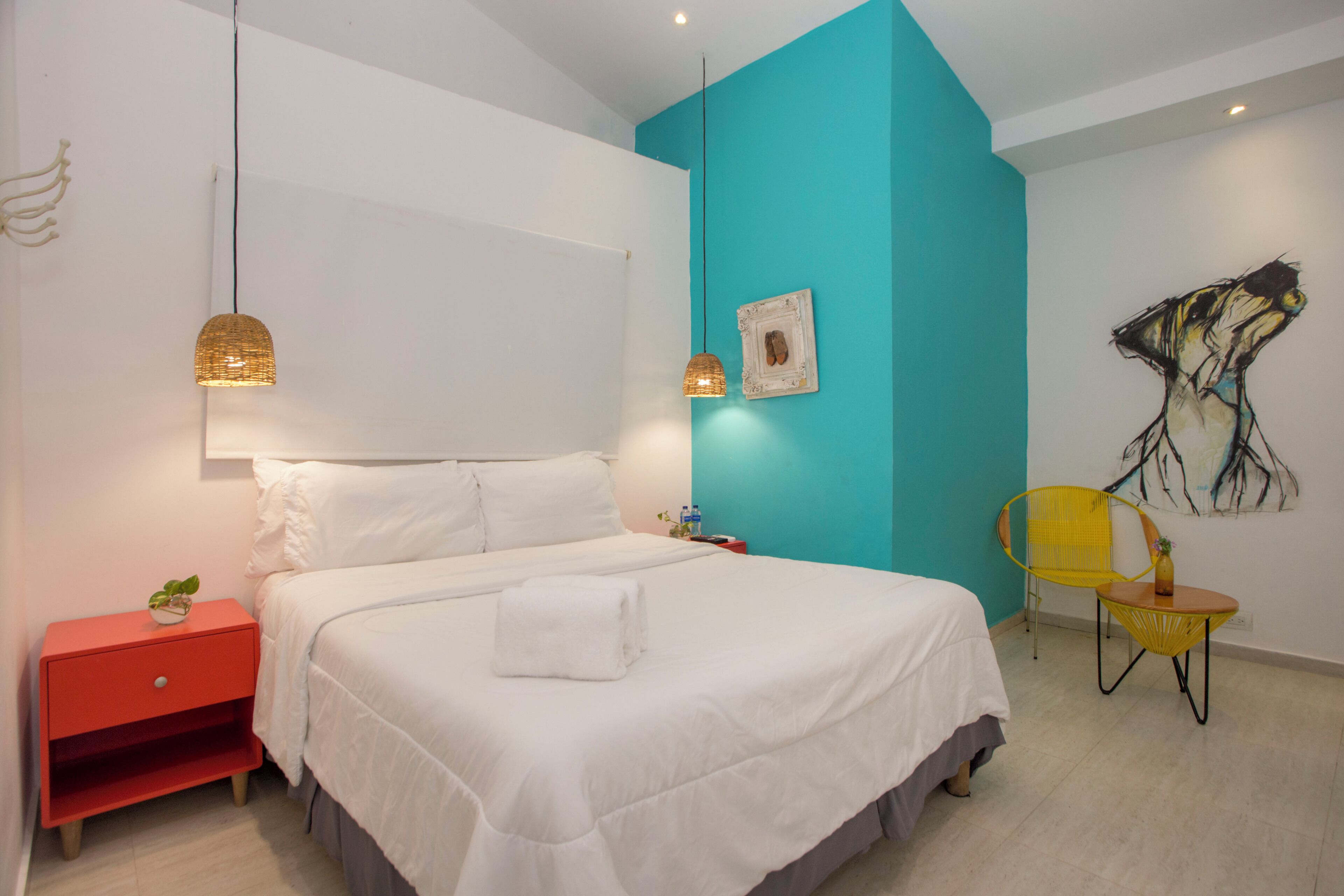 A modern bedroom with a bed, a red nightstand, a yellow chair, and a painting on the wall.
