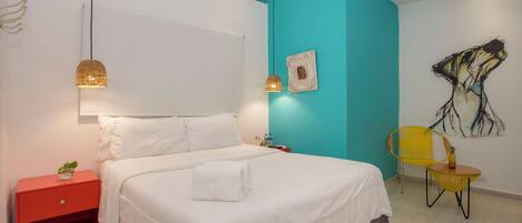 A modern bedroom with a bed, a red nightstand, a yellow chair, and a painting on the wall.