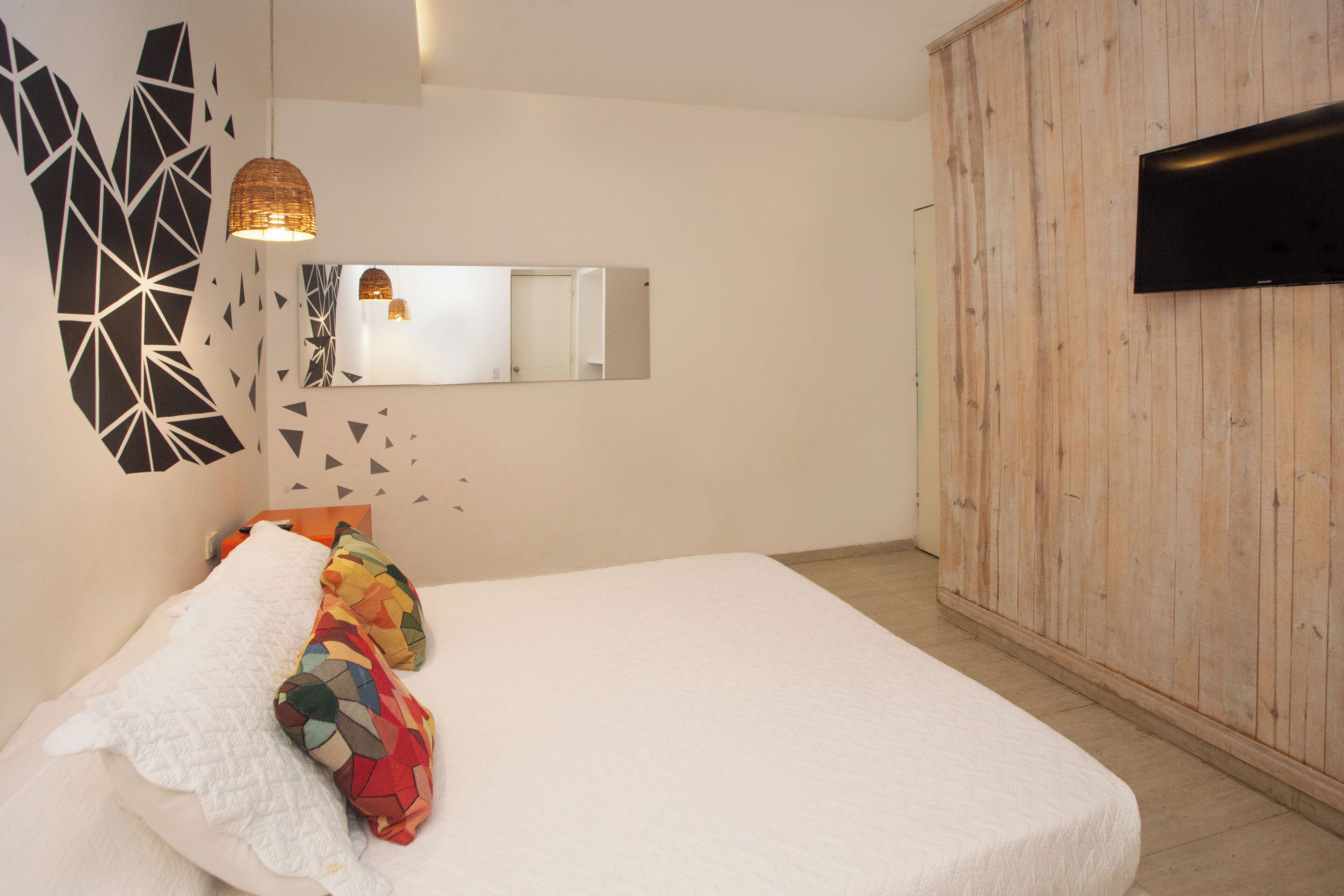 A bedroom with a bed, a mirror, a television, and a wooden wall.