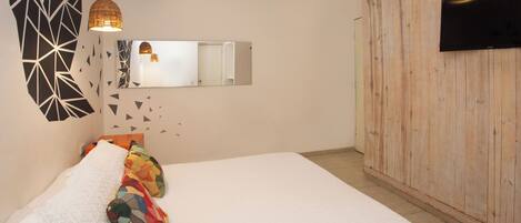 A bedroom with a bed, a mirror, a television, and a wooden wall.