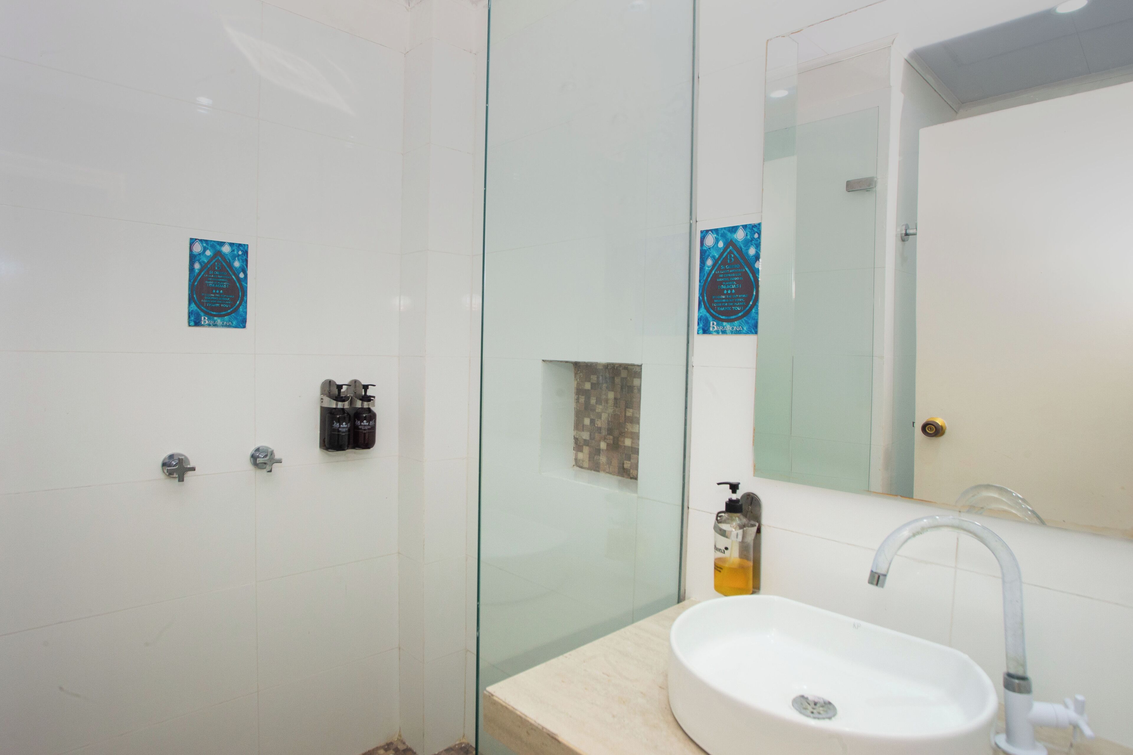A modern bathroom with a glass shower enclosure, a sink with a mirror, and two soap dispensers on the wall.
