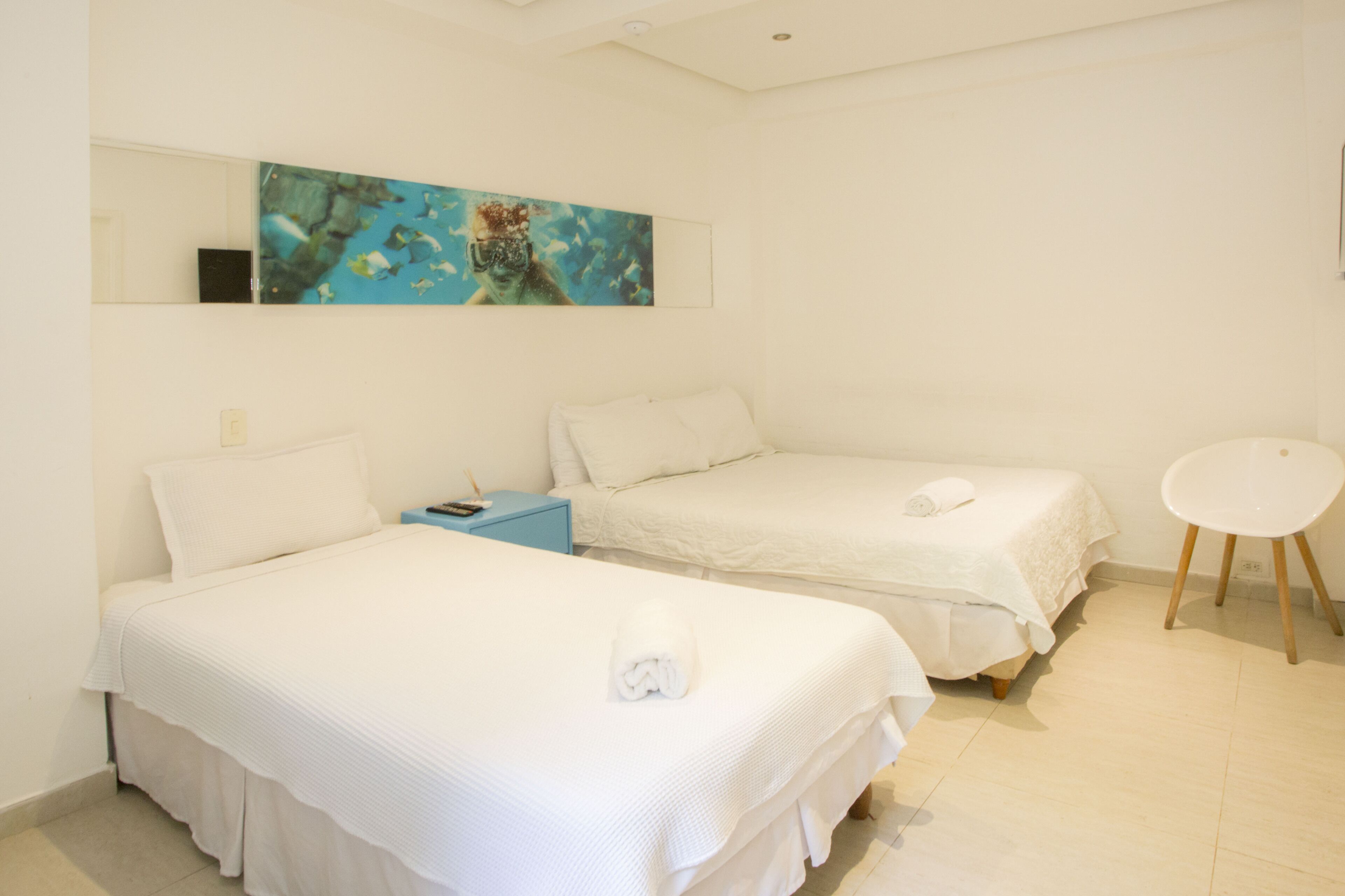 Una camera d'albergo con due letti singoli, un tavolino, una sedia e un quadro appeso al muro.