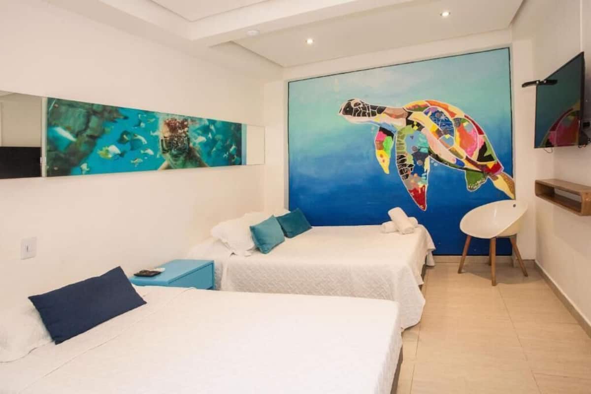 A hotel room with two beds, a large mural of a sea turtle, a TV, and a chair.