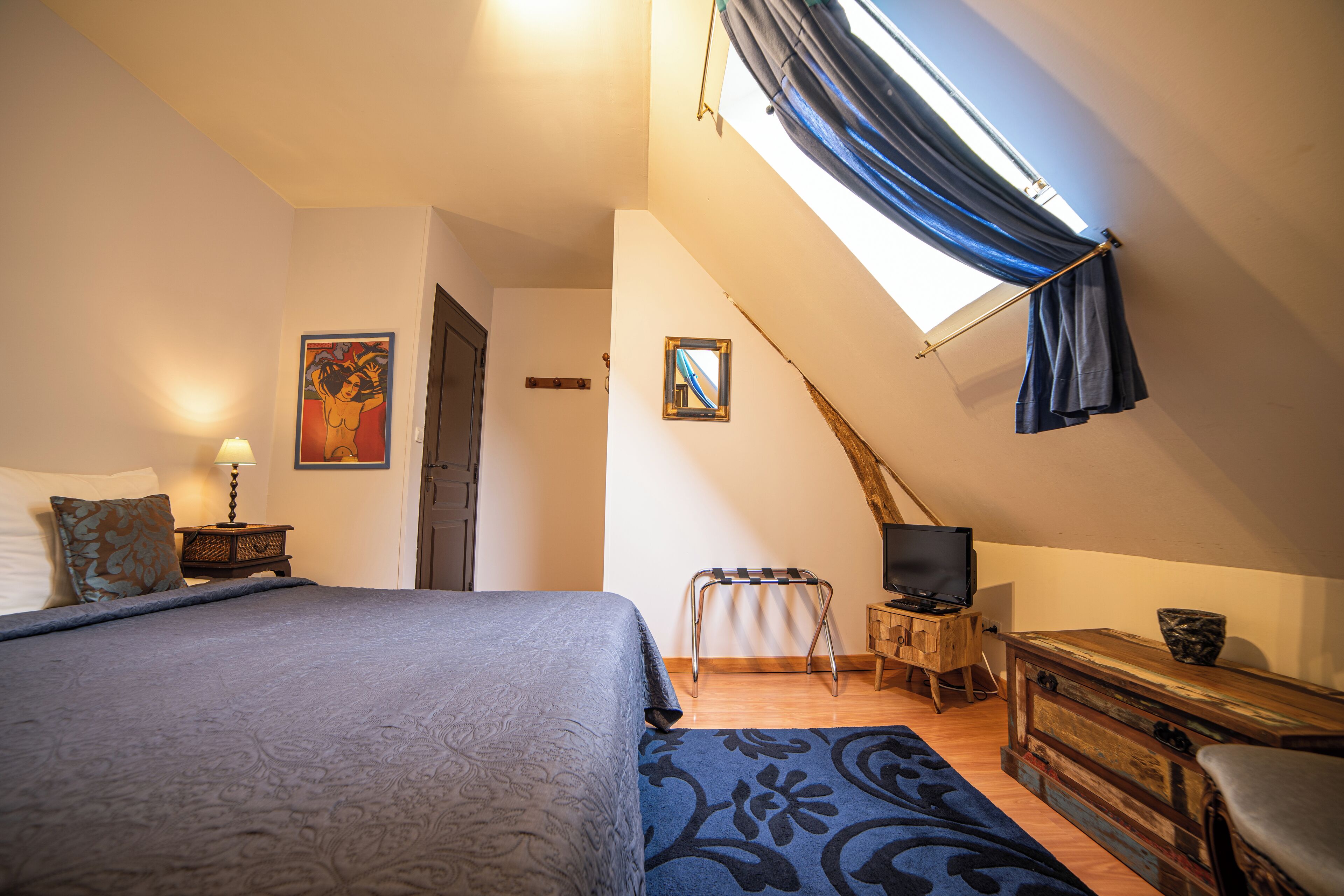 A bedroom with a bed, a TV, a small table, a chair, and a window with curtains.
