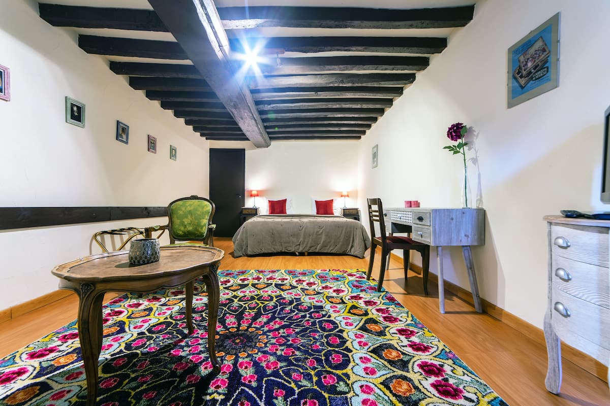 Una habitación con cama, escritorio, silla, mesa y un tapete colorido.