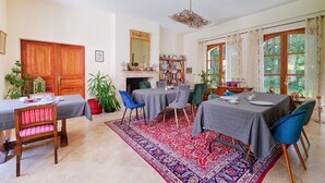 Un coin repas avec une table dressée pour quatre personnes, entourée de chaises, un tapis à motifs et une bibliothèque en arrière-plan.