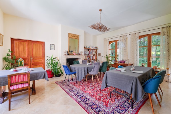 Un coin repas avec une table dressée pour quatre personnes, entourée de chaises, un tapis à motifs et une bibliothèque en arrière-plan.