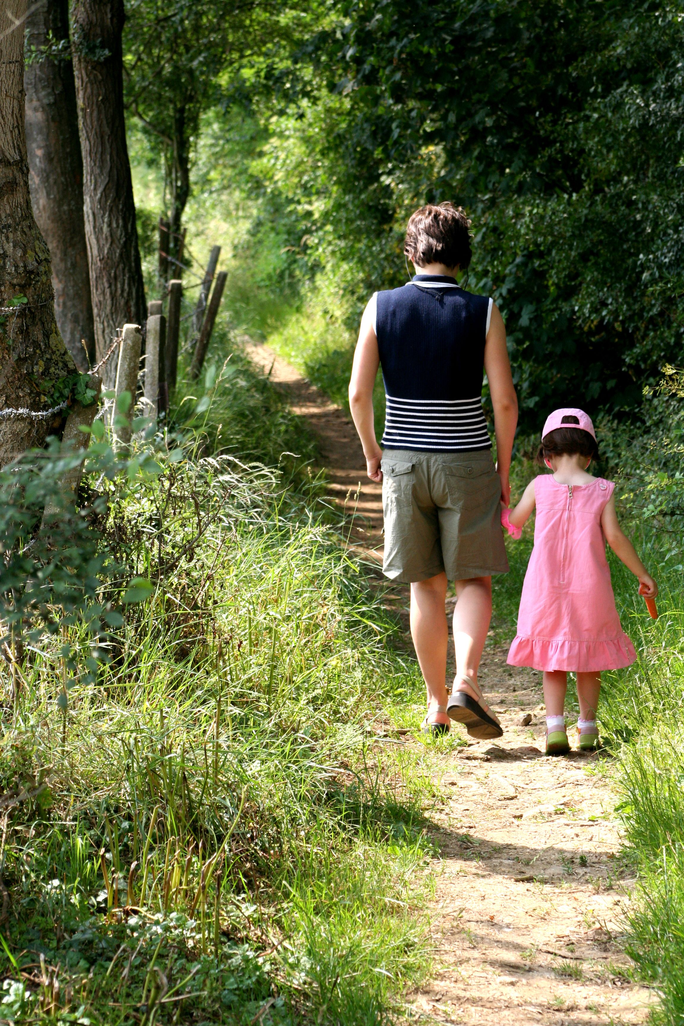 A person and a child walking on a dirt path surrounded by greenery.