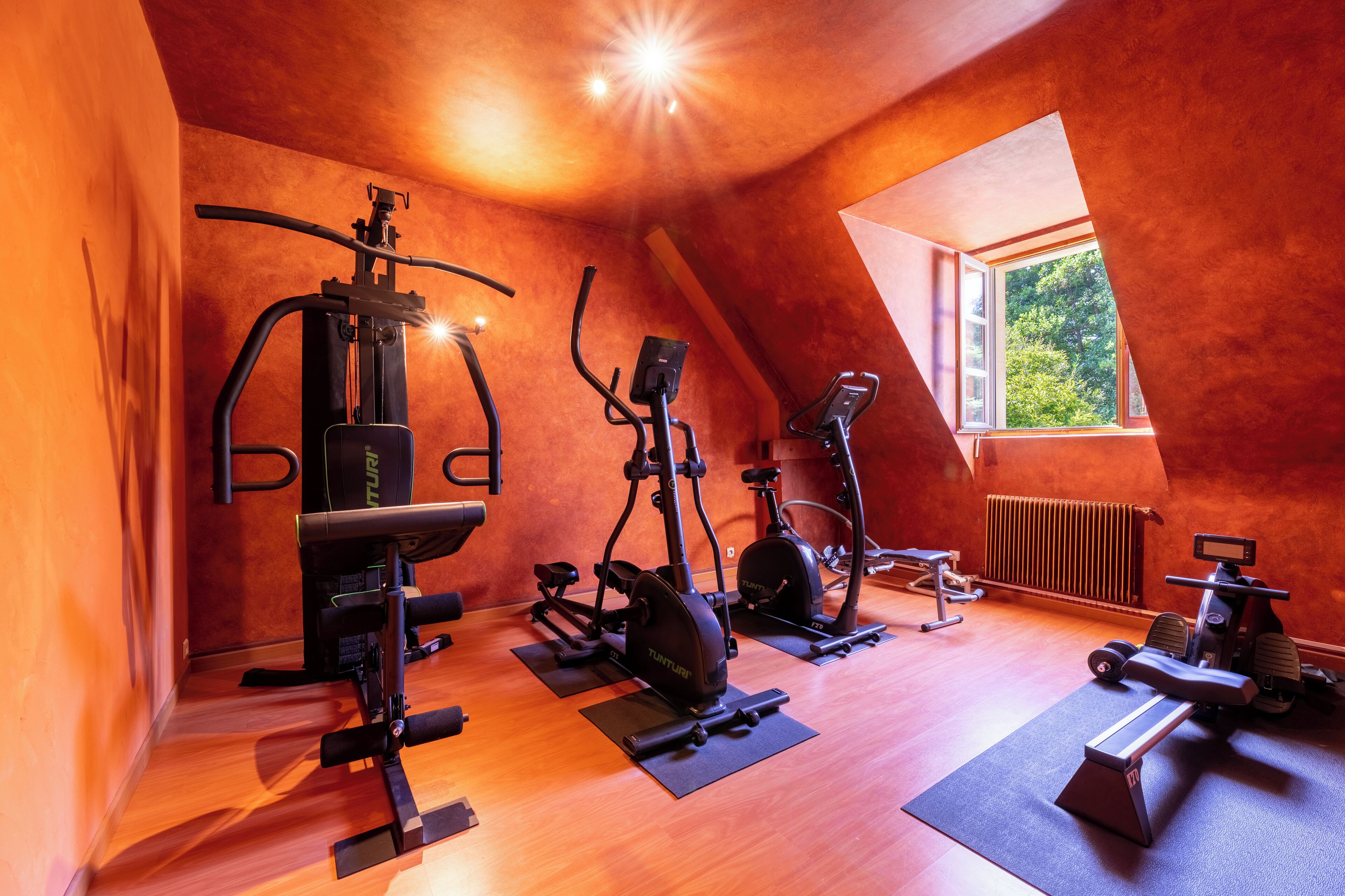 Un gimnasio con diferentes equipos de ejercicio, techo inclinado y una ventana que proporciona luz natural.