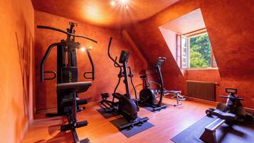 Un gimnasio con diferentes equipos de ejercicio, techo inclinado y una ventana que proporciona luz natural.