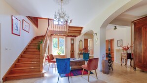 Un vaste espace de vie agrémenté d’un escalier en bois, d’un lustre et d’une table à manger avec des chaises.