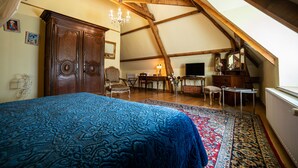 Une chambre à coucher avec un grand lit, des poutres apparentes en bois au plafond, un lustre, un bureau et un téléviseur.