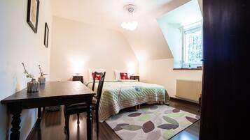 A bedroom with a bed, a desk, and a chair. There is a window with a view of trees and a radiator on the wall.