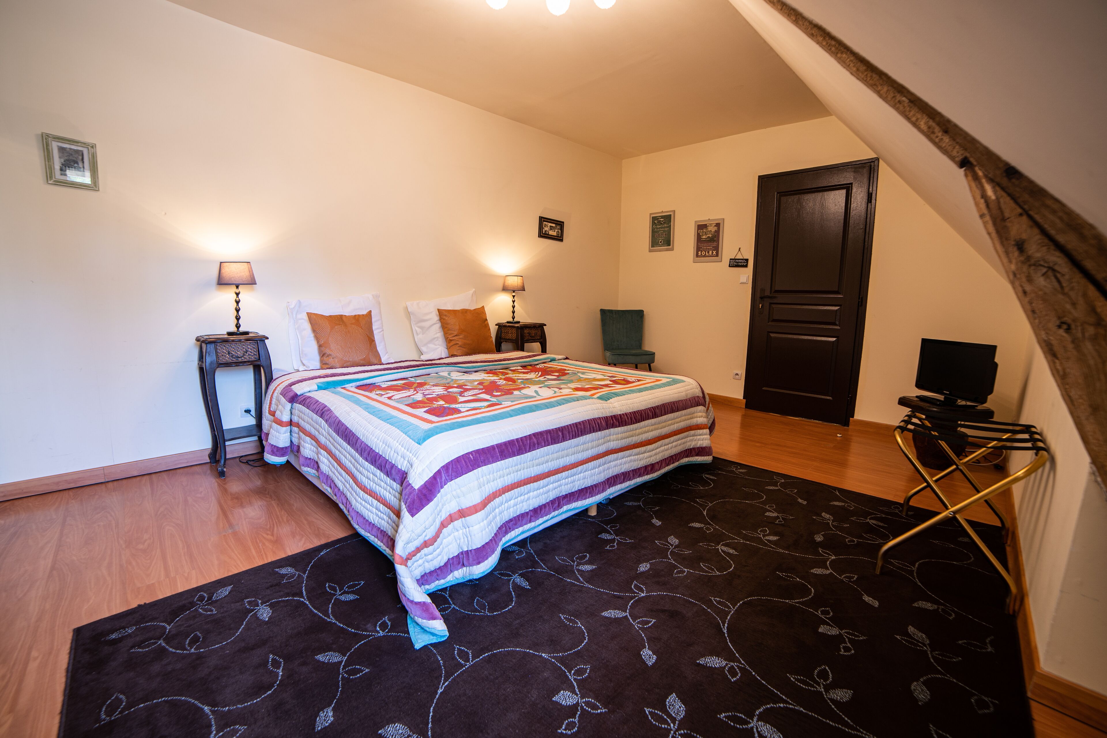 A bedroom with a bed, two bedside tables with lamps, a chair, a door, and a television on a stand.