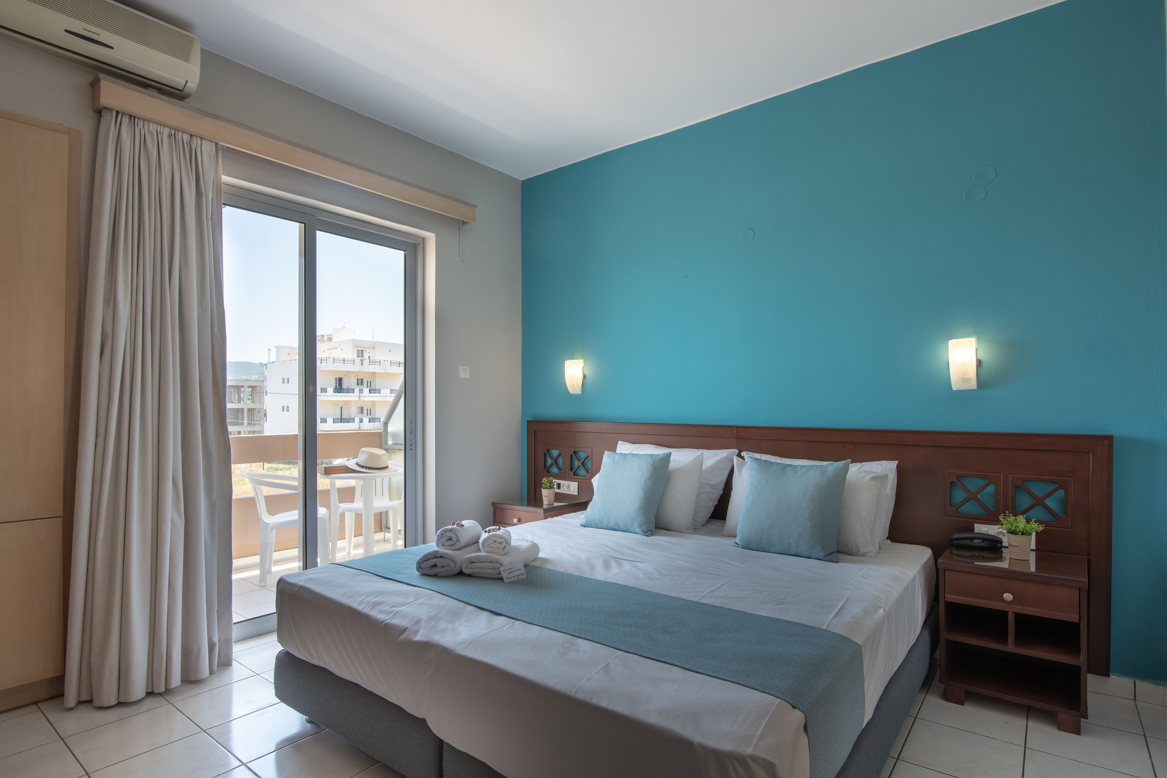 A hotel room with a large bed, a nightstand, a window with curtains, and a view of the outside.