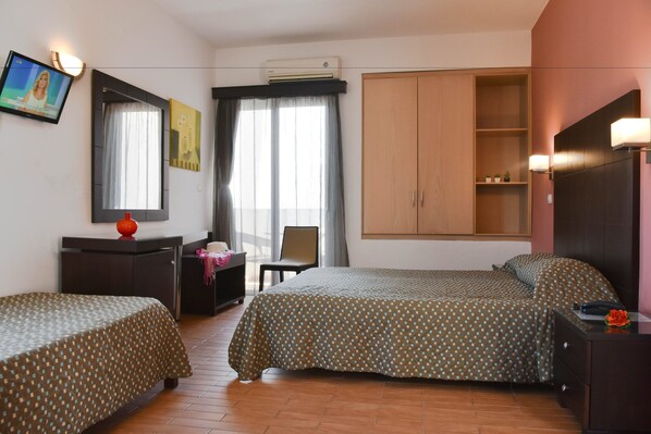 Habitación de hotel con dos camas, un escritorio, una silla, un armario y un televisor.