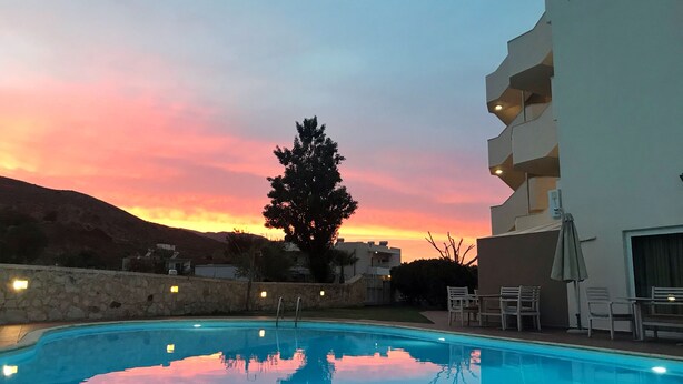 A swimming pool with a sunset view, a stone wall, and outdoor seating. - Hotel Hermes (Kissamos)