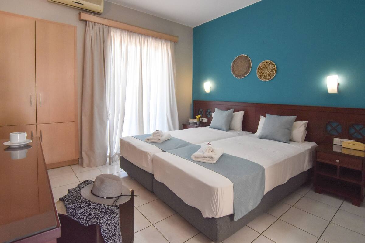 Una habitación de hotel con una cama grande, dos mesitas de noche, un armario y una ventana con cortinas.