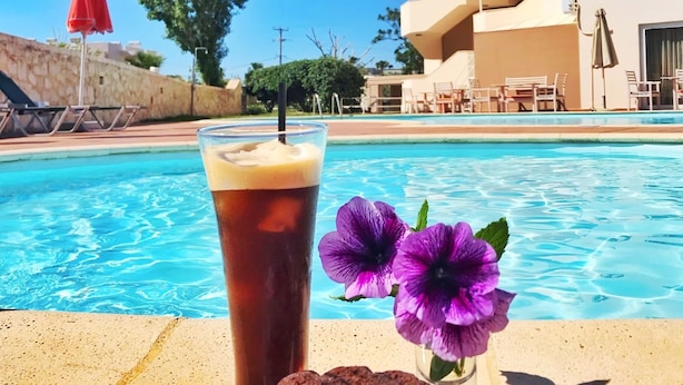 Cenário à beira da piscina com bebida, prato de comida e uma flor.