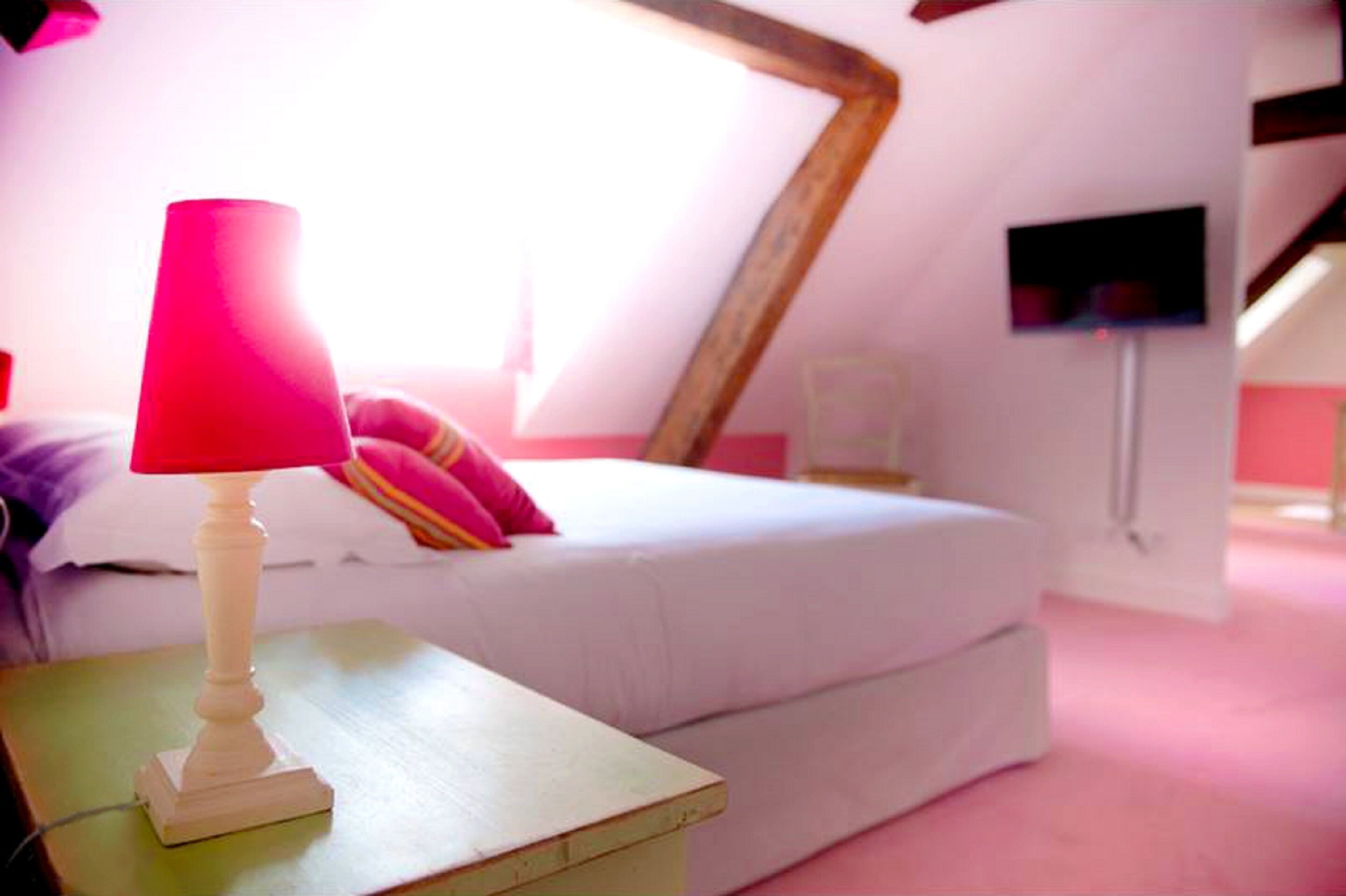 Un dormitorio con una cama, una mesita de noche, una lámpara y un televisor montado en la pared.