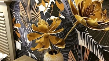 Una habitación con un amplio papel tapiz floral y un jarrón con flores sobre una mesa.