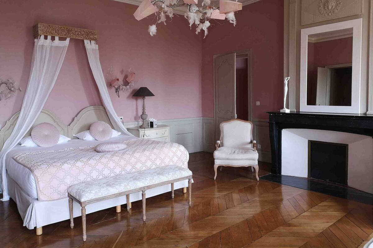 Une chambre à coucher avec un lit à baldaquin, une table de chevet, une chaise et une cheminée.