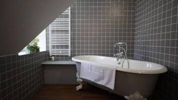 A bathroom with a freestanding bathtub, tiled walls, and a window with blinds.