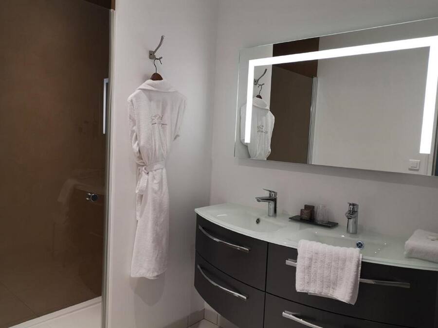 Een moderne badkamer met een douchecabine van glas, een witte badjas hangend aan een haak, een wastafel met spiegel en een handdoek op het aanrecht.