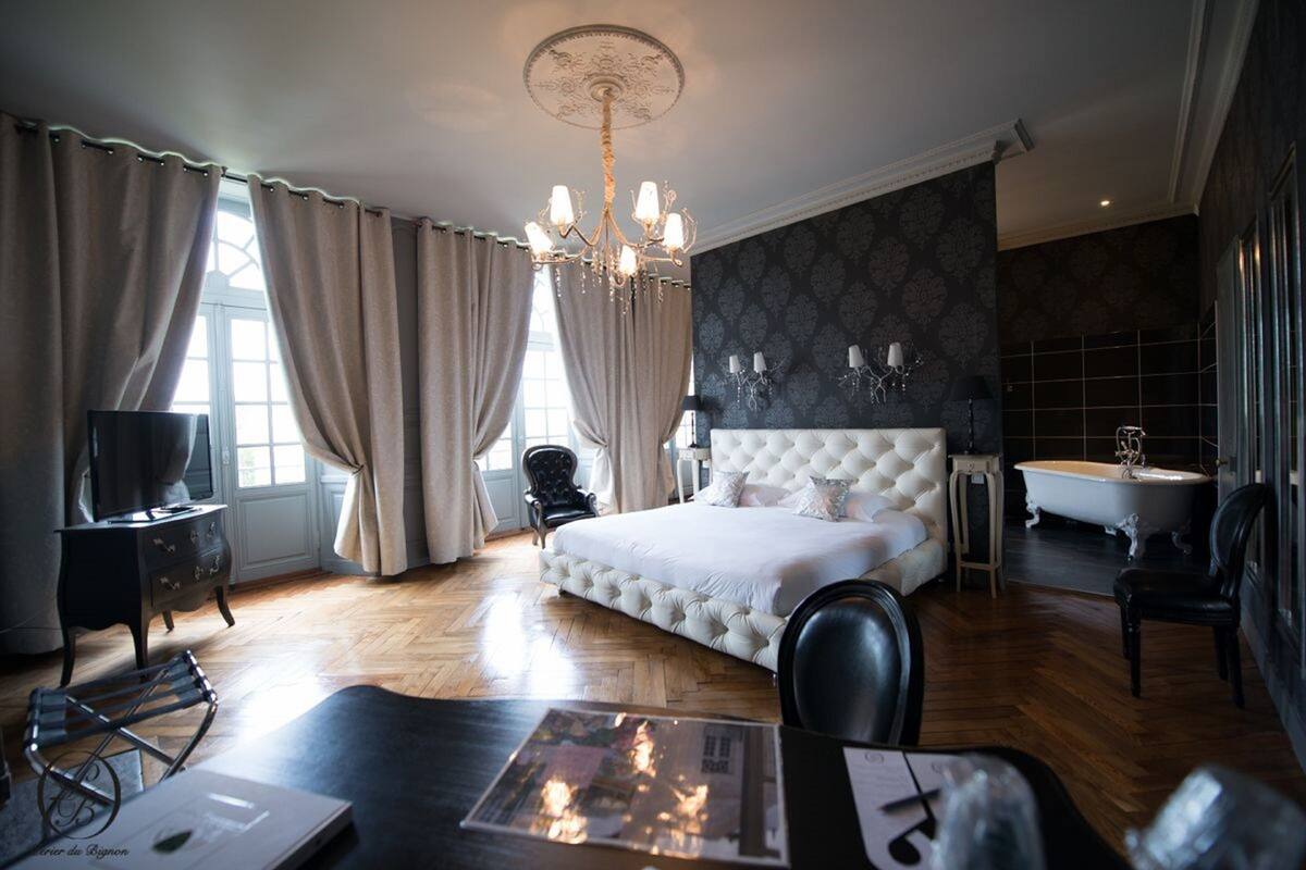 Une chambre spacieuse avec un grand lit, un lustre, une coiffeuse avec un miroir et une baignoire.