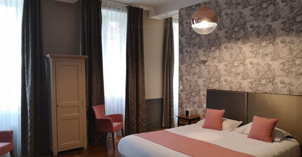 A hotel room with a large bed, a wardrobe, a chair, and a nightstand.