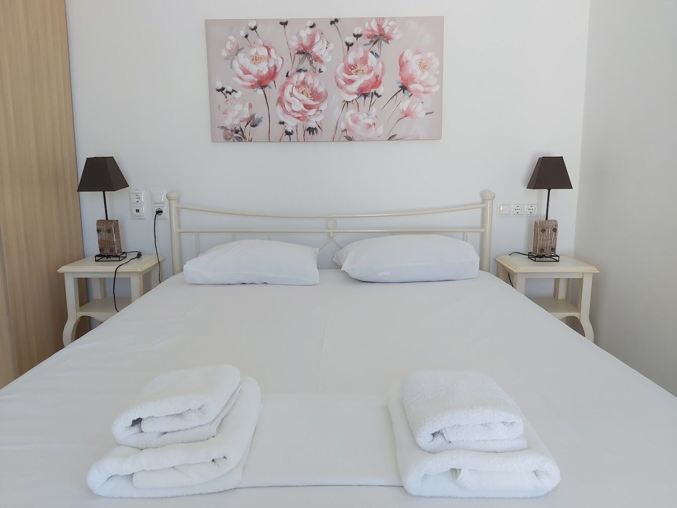 A neatly made bed with white linens and two folded towels at the foot of the bed.