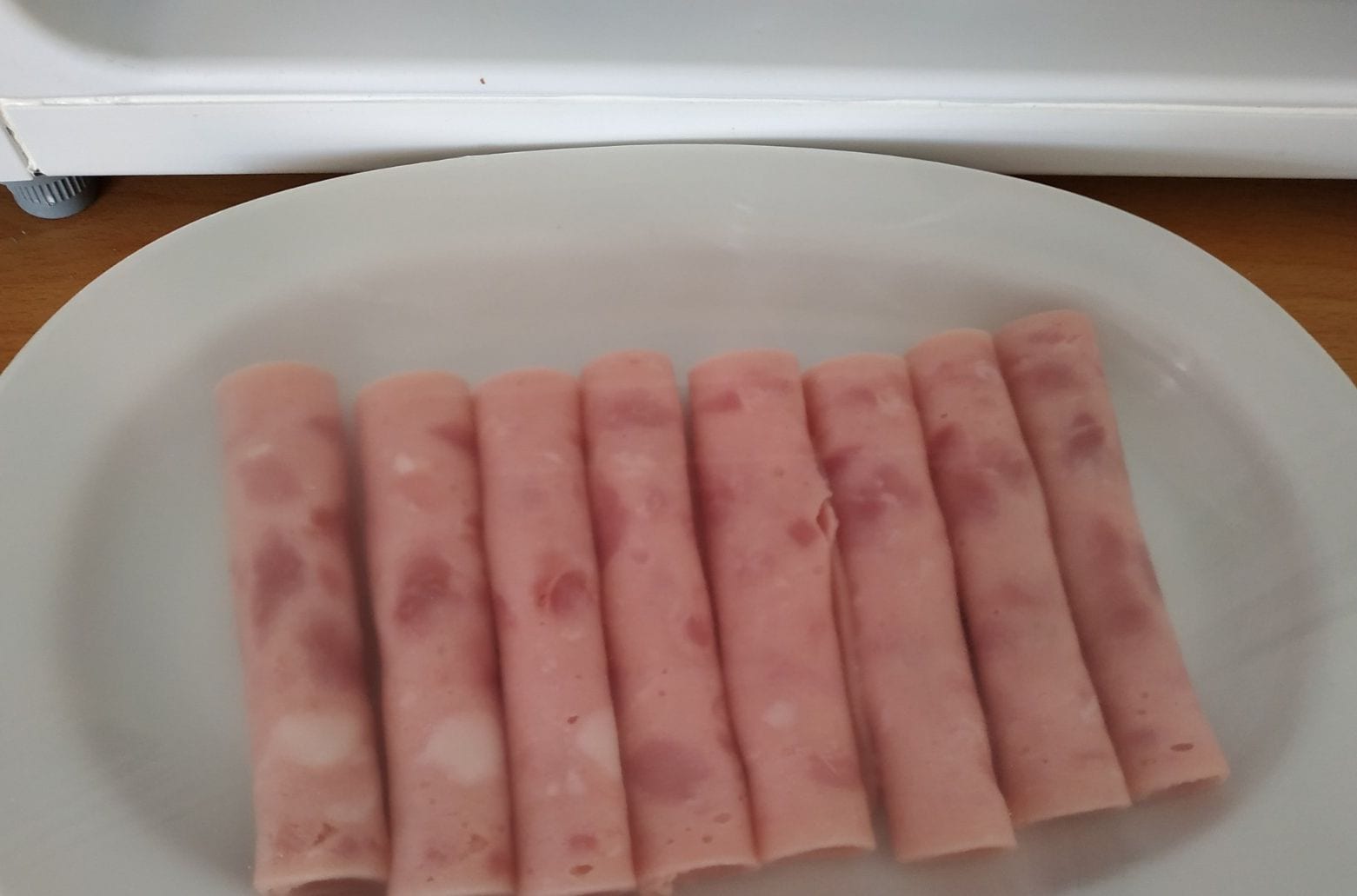 A white plate with several pink cylindrical items on a wooden surface.