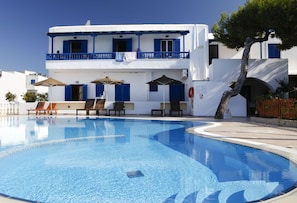A hotel with a swimming pool, blue-framed windows, and outdoor seating. - Anna Studios (Naxos)