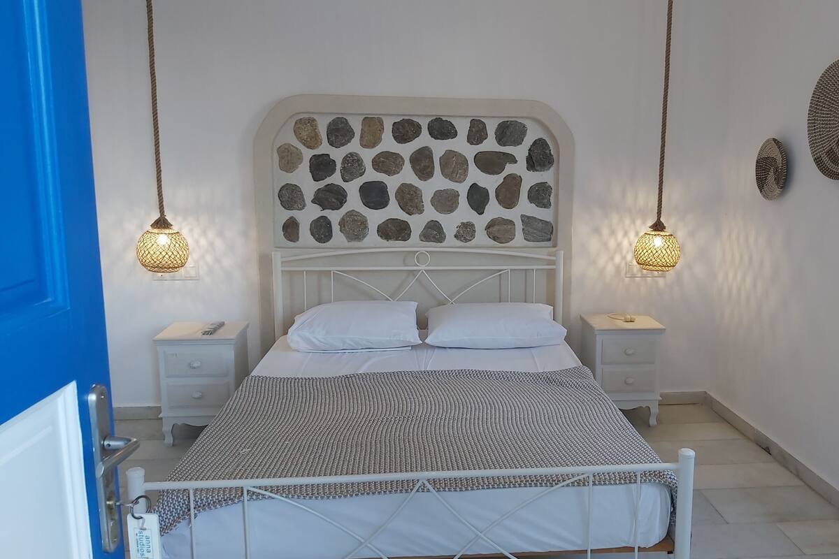 A bedroom with a white bed, two bedside tables, a white headboard with a stone pattern, and two hanging lamps.