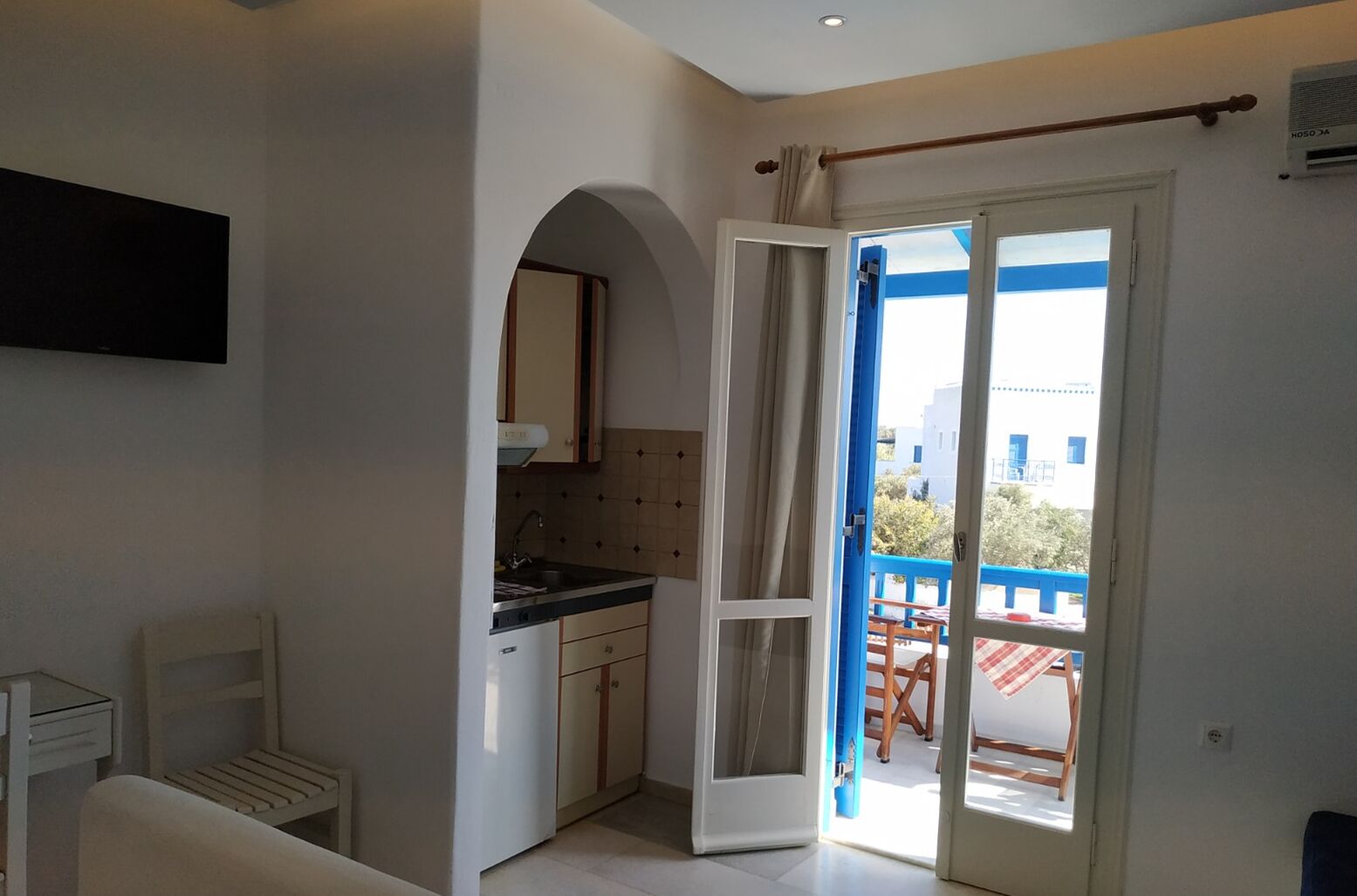 Eine kompakte Küche mit Einbauofen, ein Essbereich mit Tisch und Stühlen sowie eine Glastür, die auf einen Außenbalkon führt.