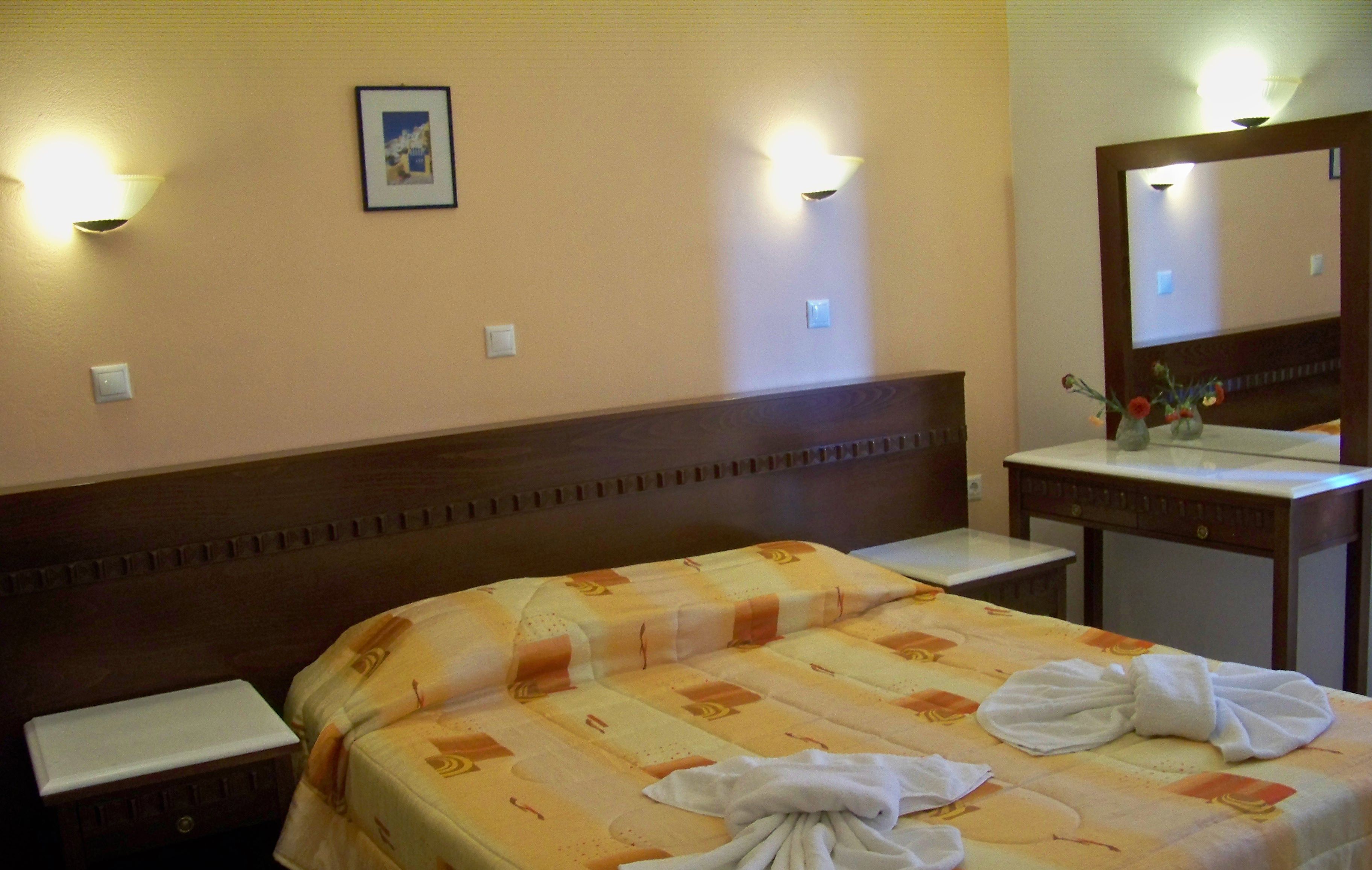Une chambre d’hôtel avec un lit bien fait, une table de chevet, un petit bureau avec un miroir et des lampes fixées au mur.