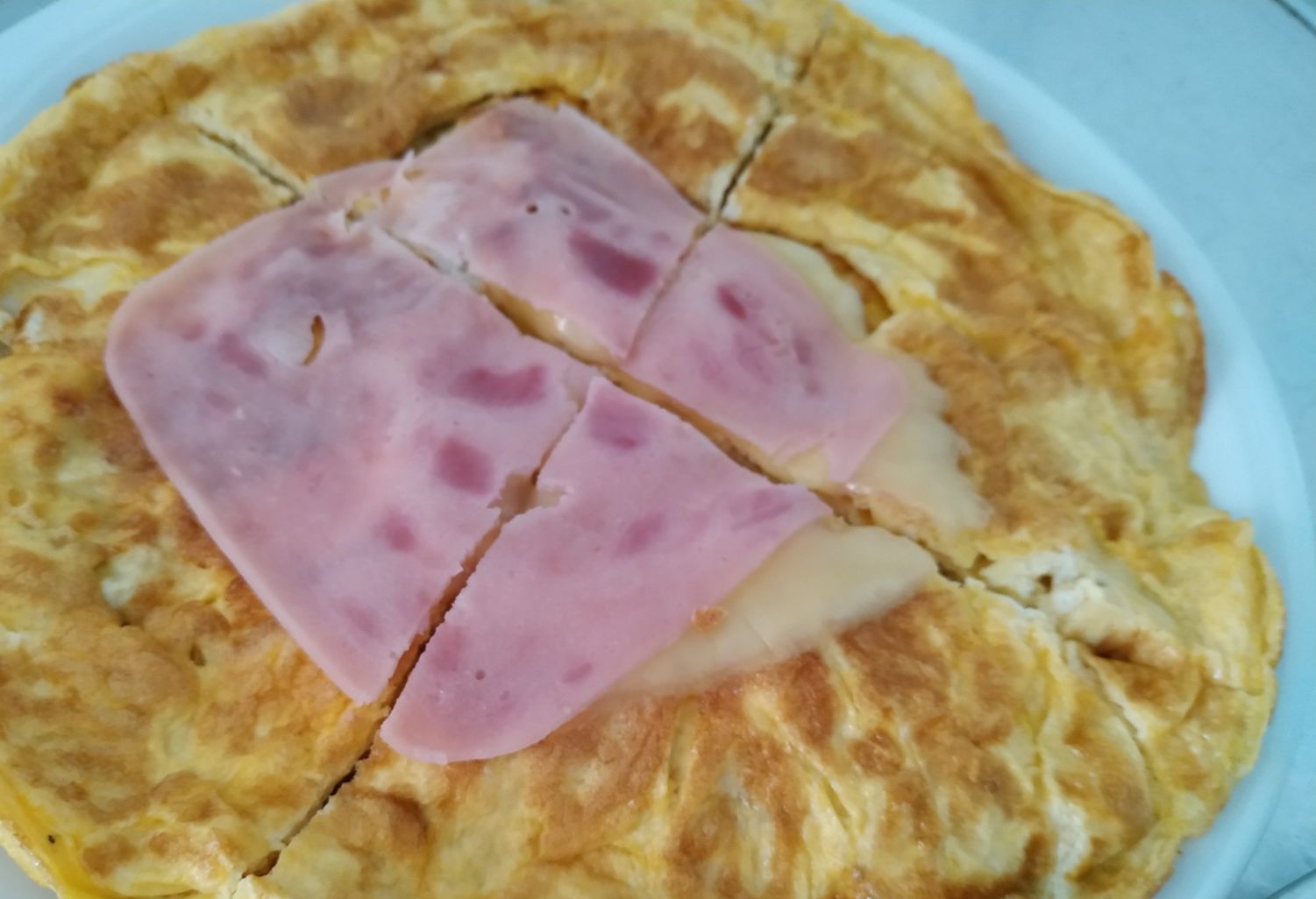 A plate with a savory dish, possibly a type of omelette or frittata, topped with slices of ham.
