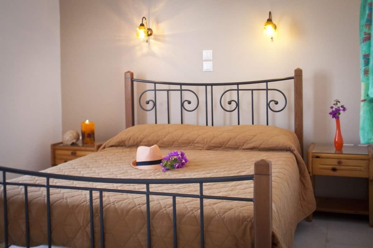 A neatly made bed with a quilted cover, a bedside table with a vase of flowers, and wall-mounted lights.