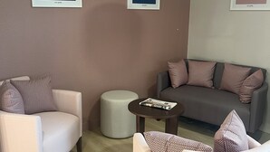 Een moderne hotelkamer met een beige bank, twee fauteuils, een kleine ronde tafel en een vloerlamp. Er hangen drie ingelijste motiverende citaten aan de muren.