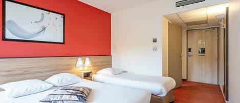 A hotel room with two beds, a red accent wall, a framed artwork, and a hallway leading to a door.