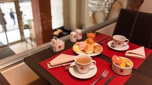 A breakfast setting with a coffee cup, pastries, and a fruit bowl on a table with a red placemat. - Icaro Suites (Buenos Aires)