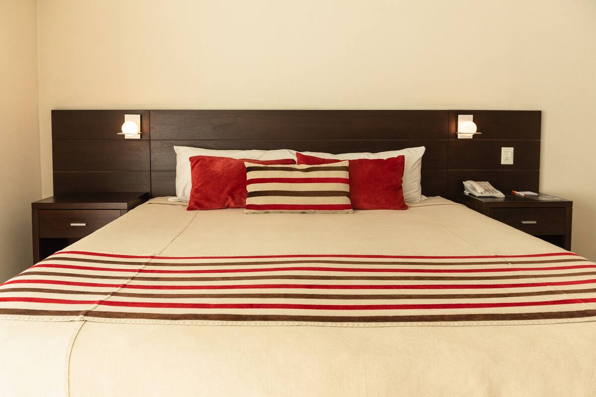 A neatly made bed with a striped bedspread, two pillows, and two bedside tables with lamps.