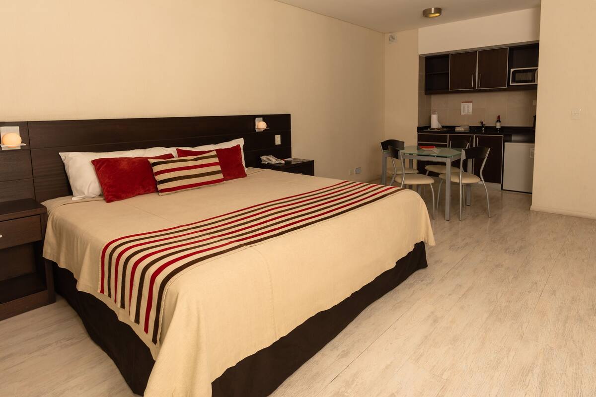 A hotel room with a large bed, a desk, and a kitchenette.