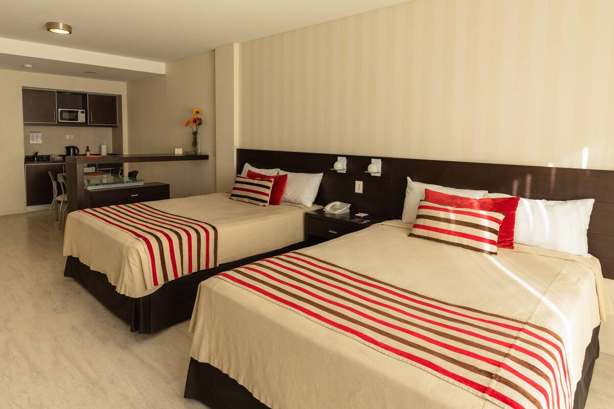 A hotel room with two beds, a desk, and a kitchenette.