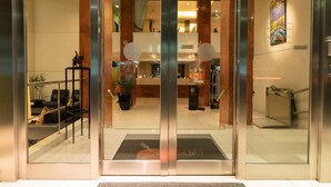 A hotel entrance with a reception desk, a seating area with a sofa and chairs, and a decorative wall piece. - Icaro Suites (Buenos Aires)